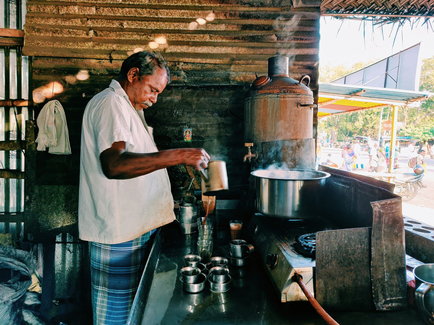 Man preparing coffee in a rustic kitchen setting with metal pots and steam.